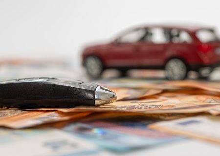 key and red toy car on pile of euro banknotes, buy or sell a car, rent a car or insurance concept